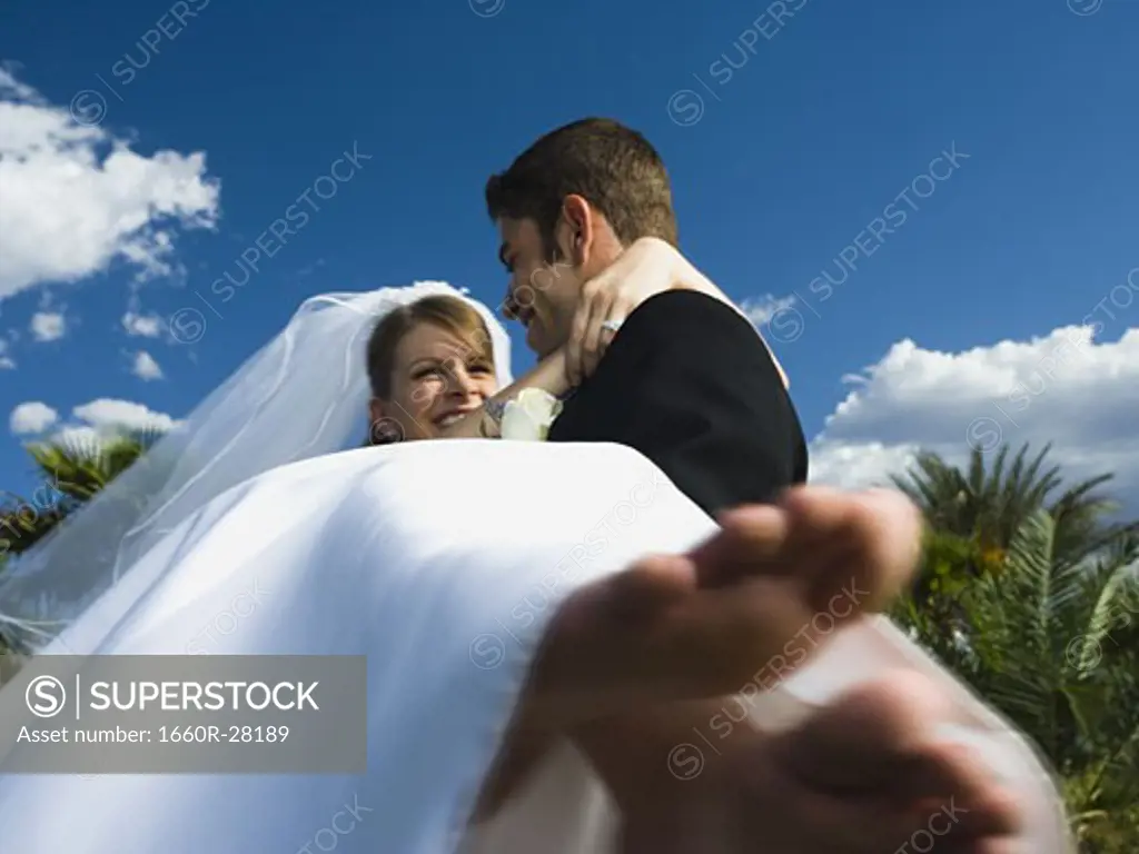 Low angle view of a young man carrying his bride and smiling