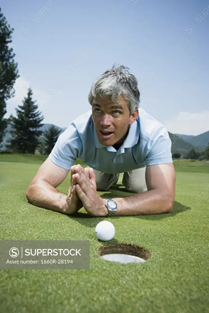 Close-up of a man kneeling in front of a golf ball near a hole and praying