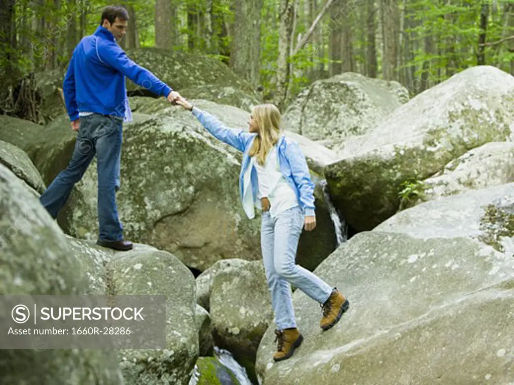 Young man helping a young woman climb a rock