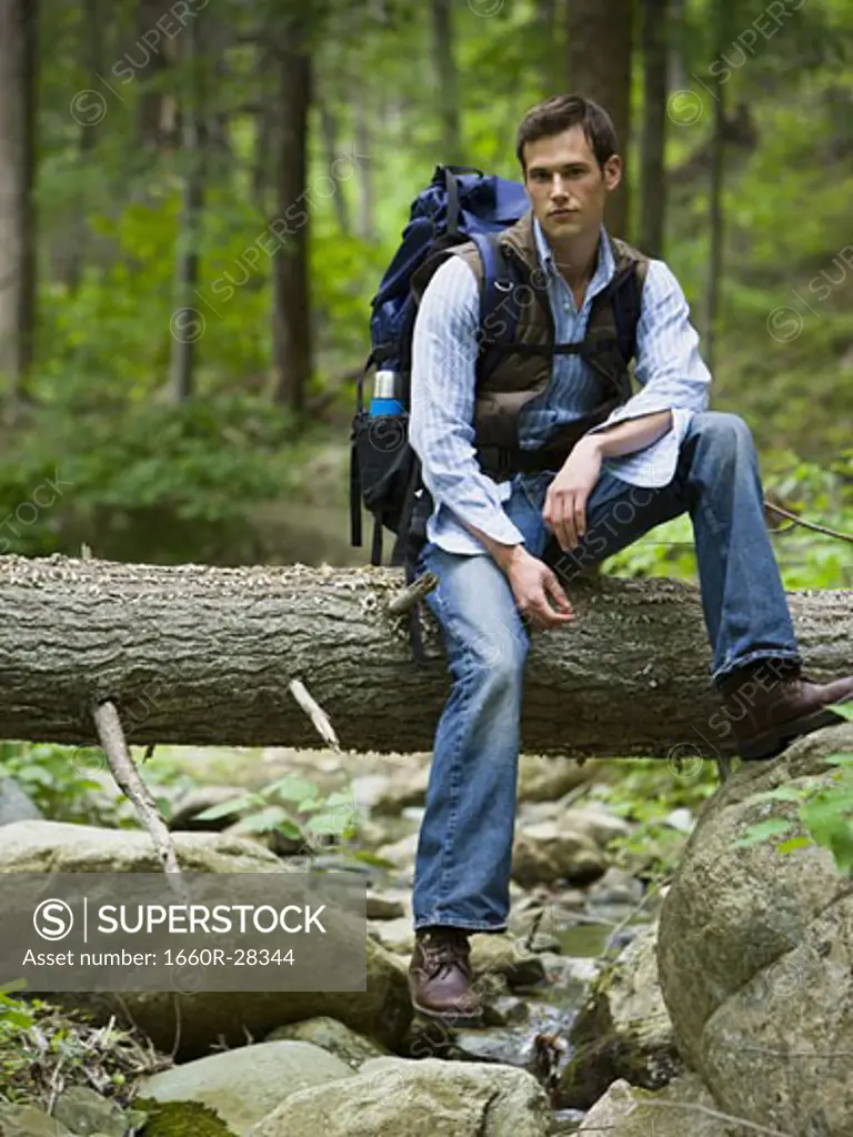 Portrait of a young man sitting on a fallen tree