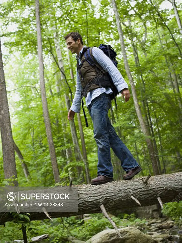 Low angle view of a young man walking on a fallen tree