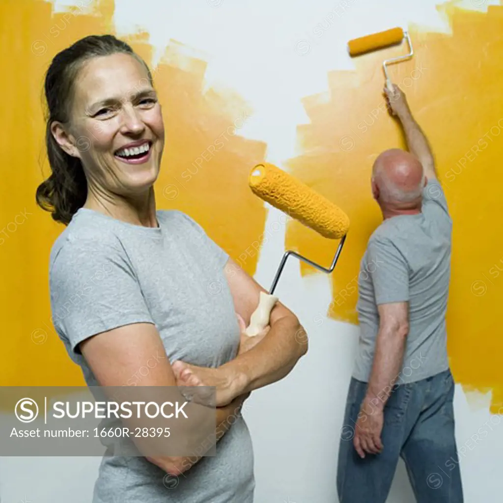 Portrait of a senior woman holding a paint roller with a senior man painting a wall