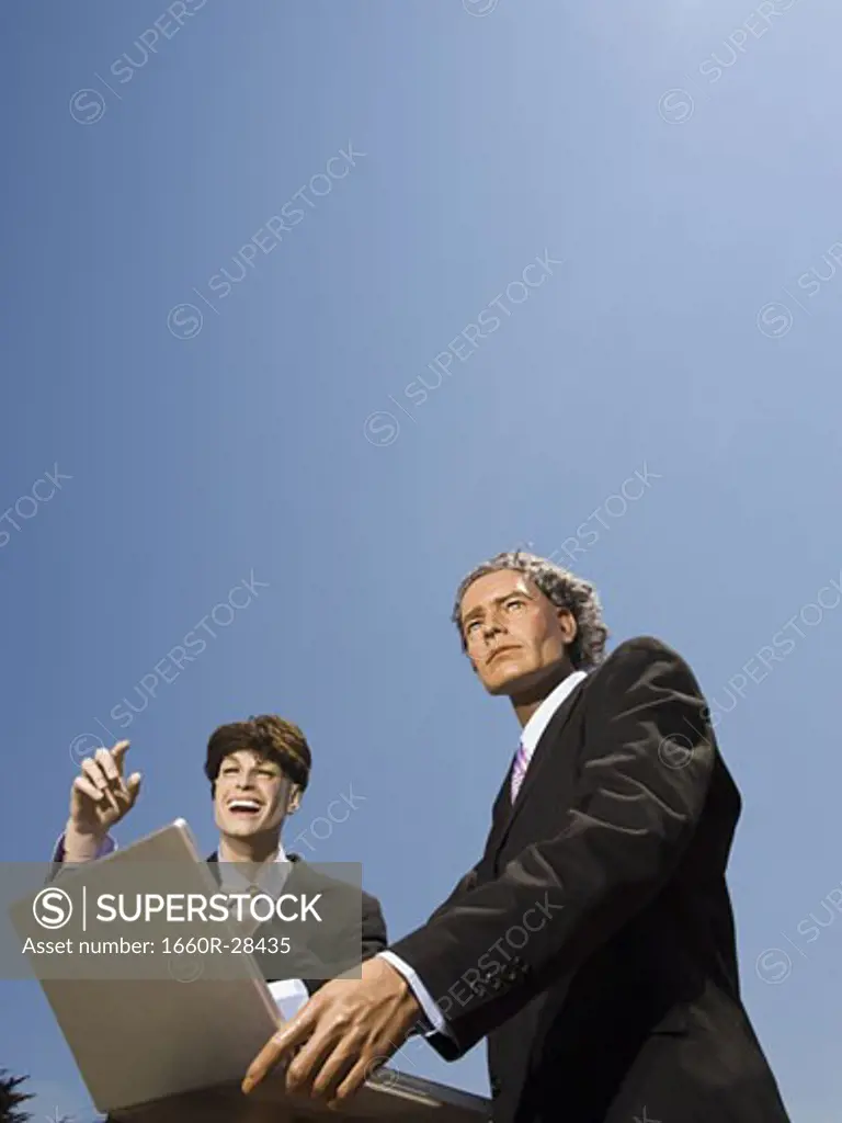 Low angle view of two mannequins portraying businessmen using a laptop