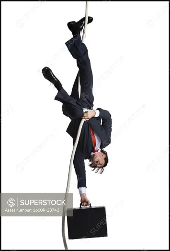 Businessman with briefcase dangling upside down from a rope