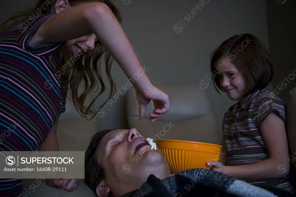 Daughters dropping popcorn into sleeping father's mouth