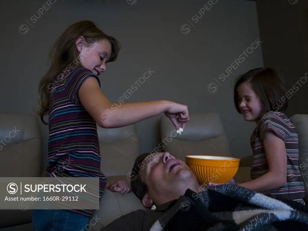 Daughters dropping popcorn into sleeping father's mouth