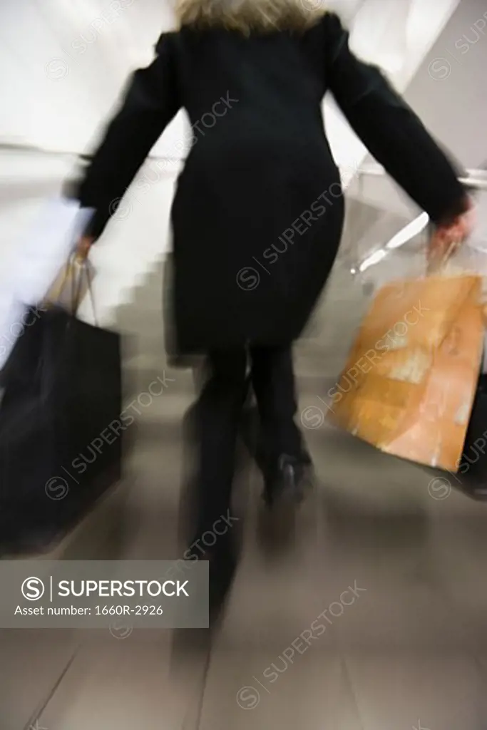 Rear view of a woman running up a staircase with shopping bags