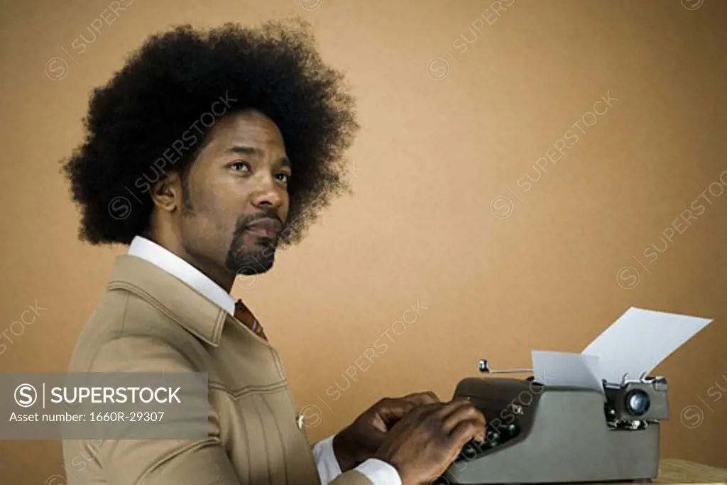 Man with an afro in beige suit typing on a typewriter