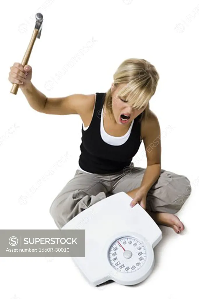 Frustrated dieting woman smashing bathroom scale with a hammer