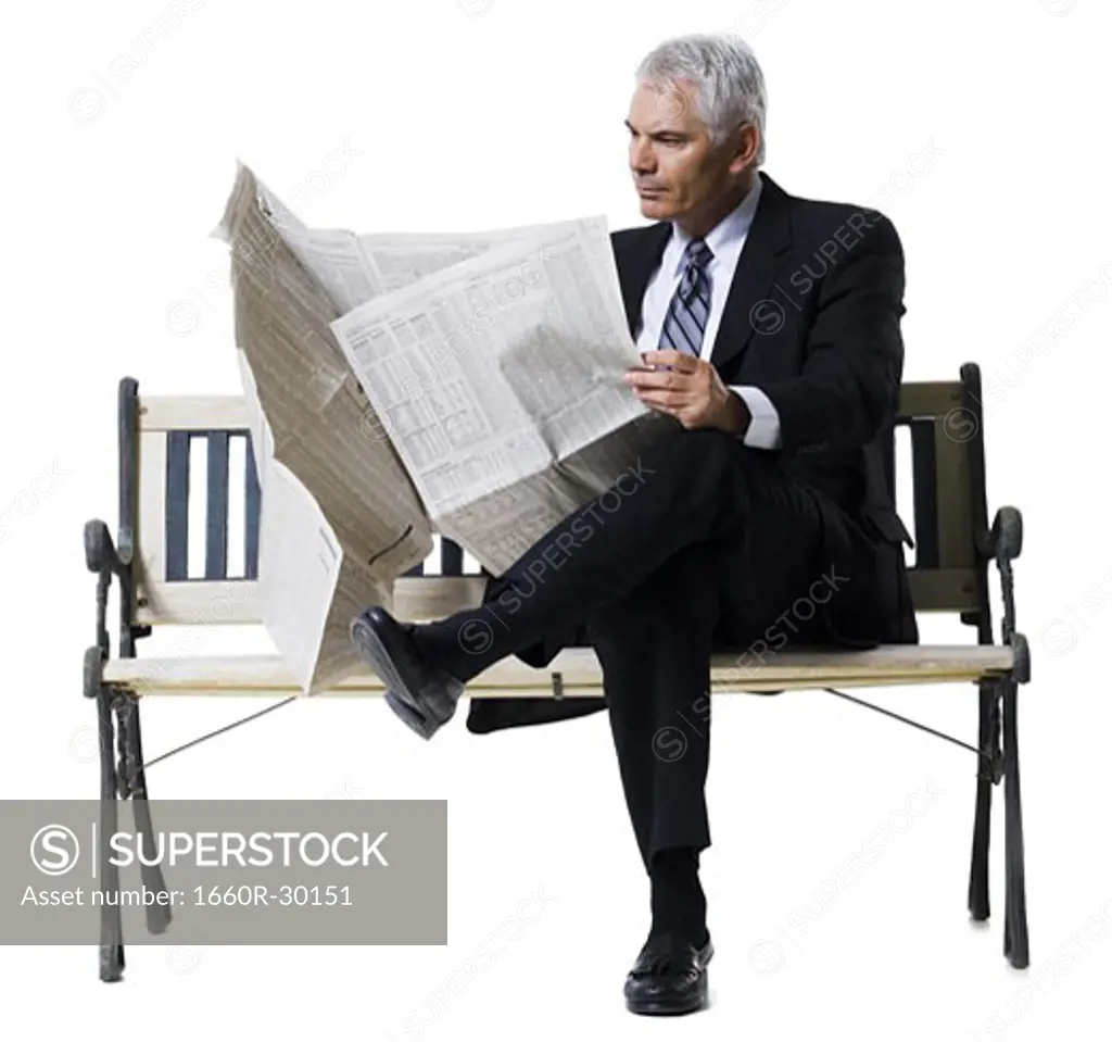 Businessman sitting on bench reading newspaper