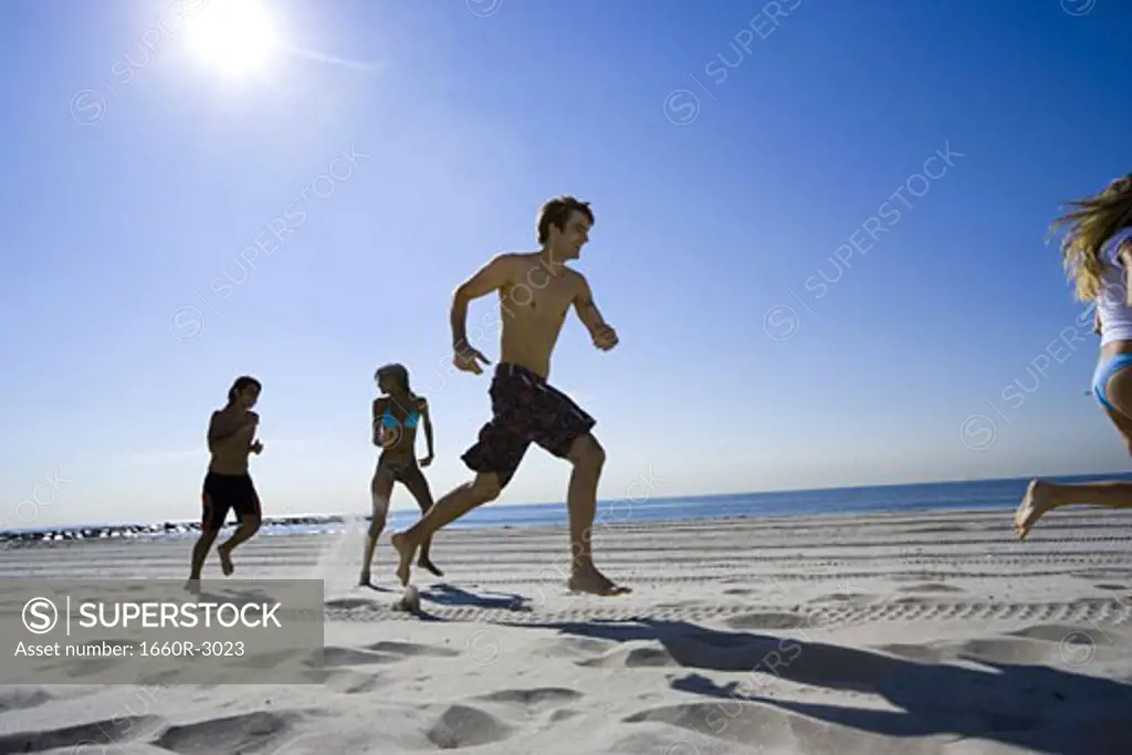 Low angle view of four young people running on the beach