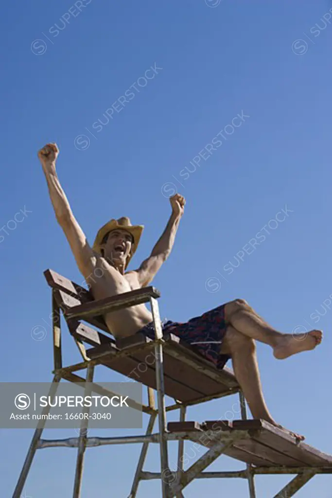 Low angle view of a young man sitting on a lifeguard chair