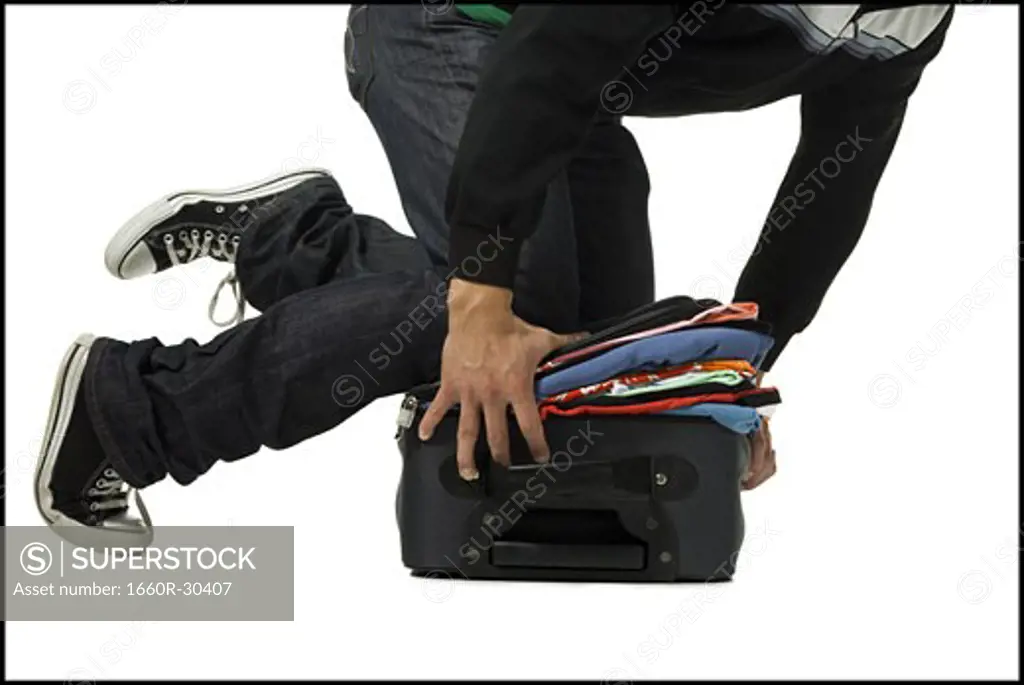 Man forcing clothes into overstuffed suitcase