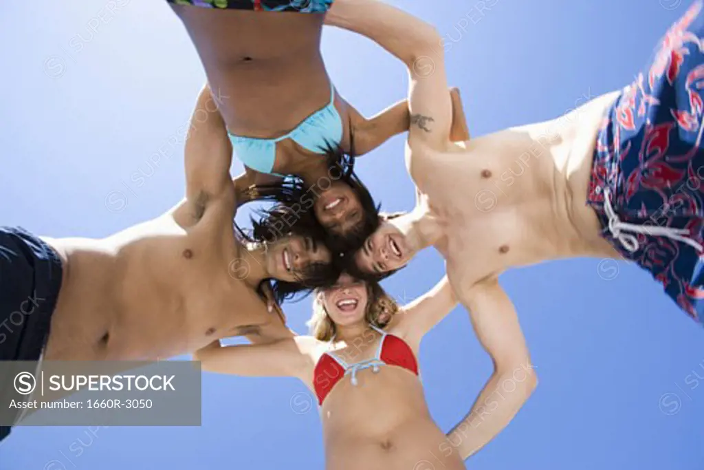 Low angle view of four young people in a huddle on the beach