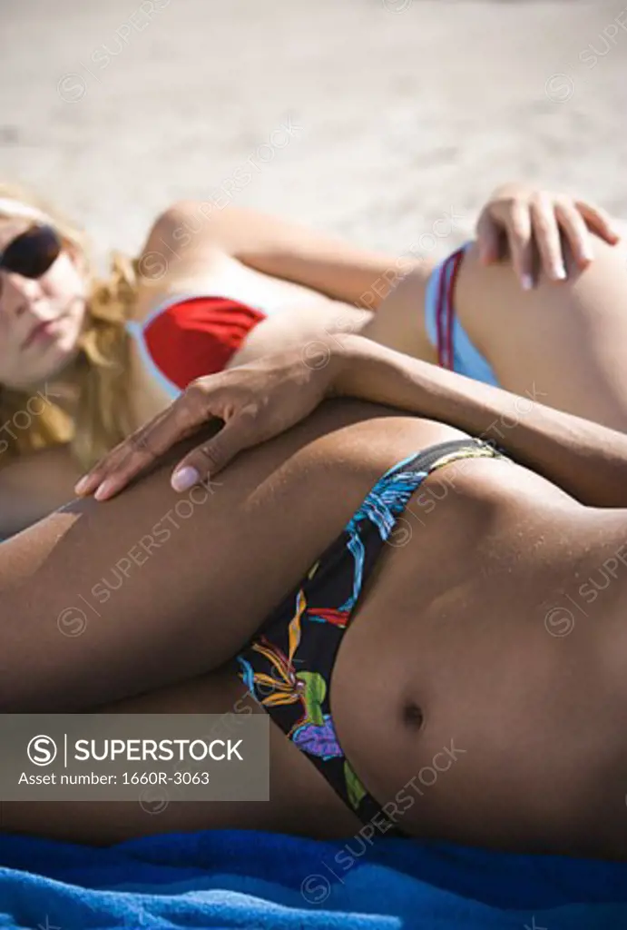 Mid section view of two young women sunbathing on the beach