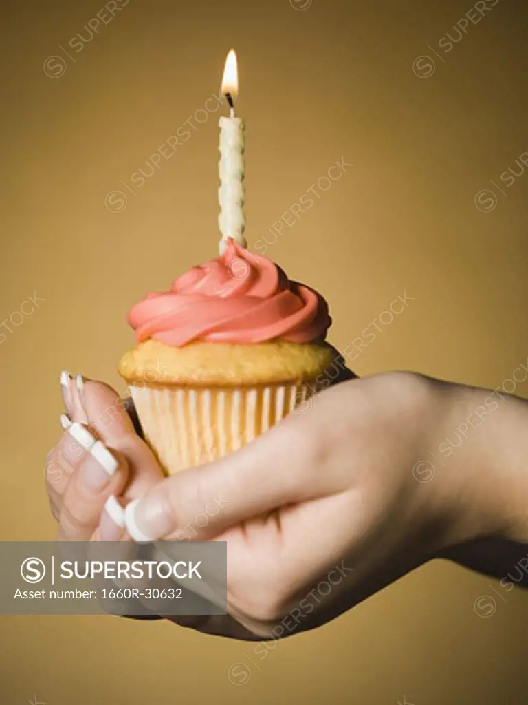 Hands holding a cupcake with one birthday candle