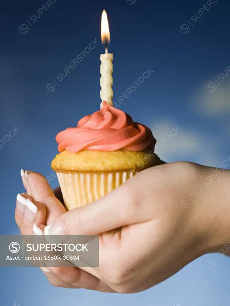 Hands holding a cupcake with one birthday candle