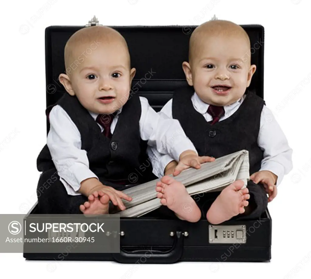 Twin baby boys in briefcase with suits and newspaper