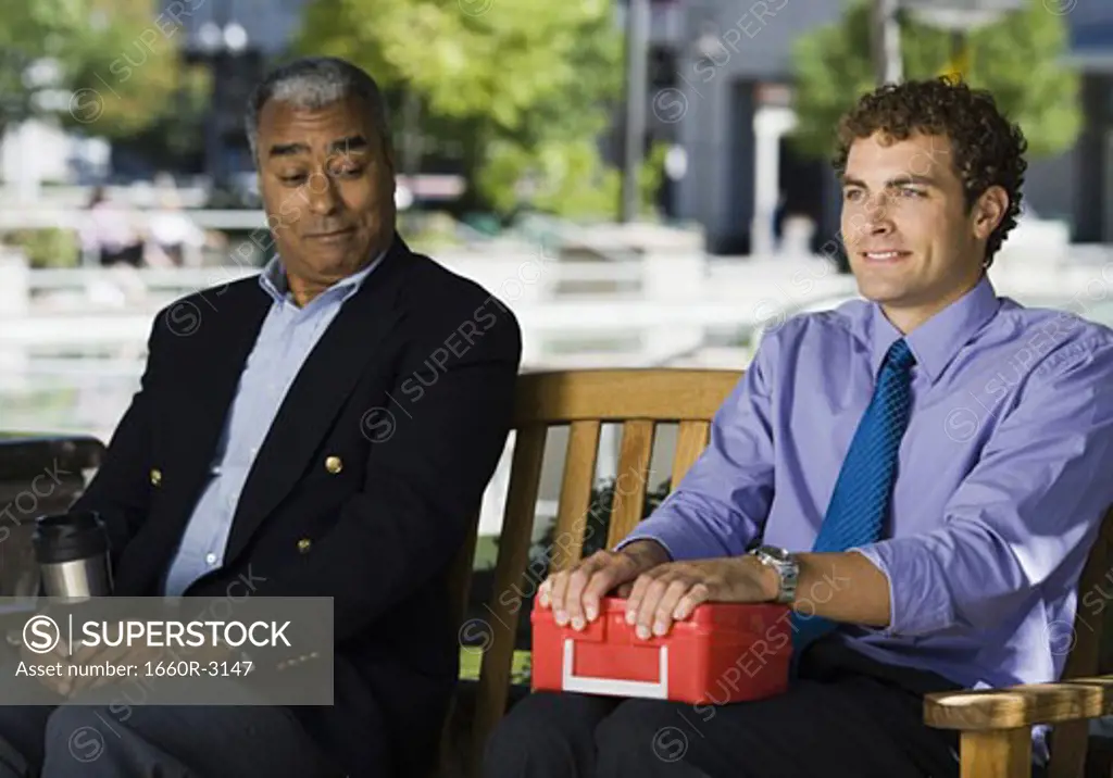 Two businessmen sitting with a lunch box and a flask