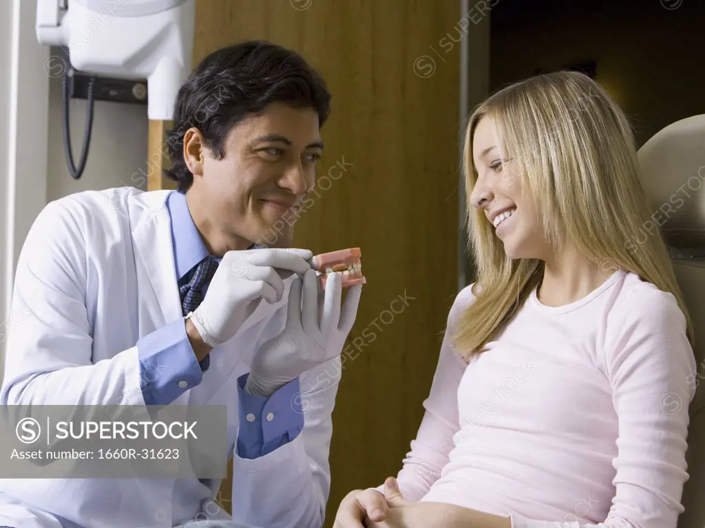 Male dentist holding false teeth talking to girl