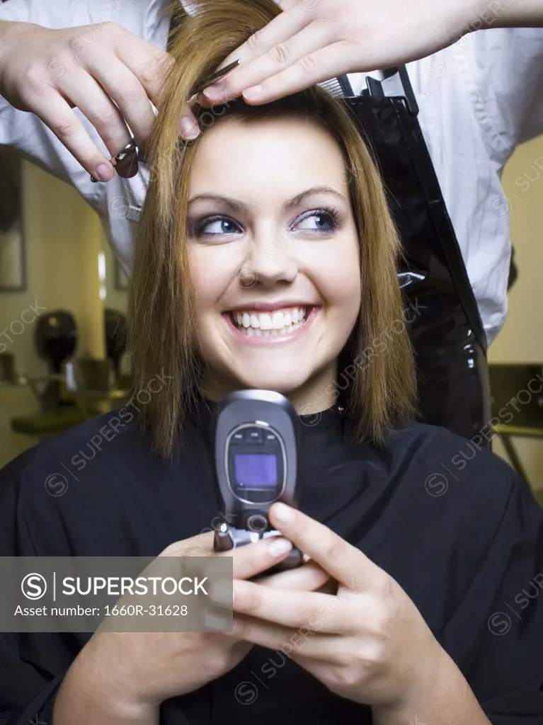 Young woman with cell phone having hair cut smiling