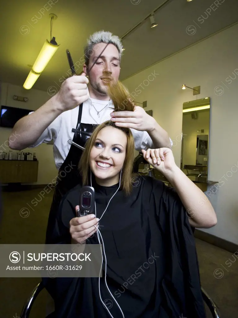 Young woman listening to music on cell phone at hairdresser's
