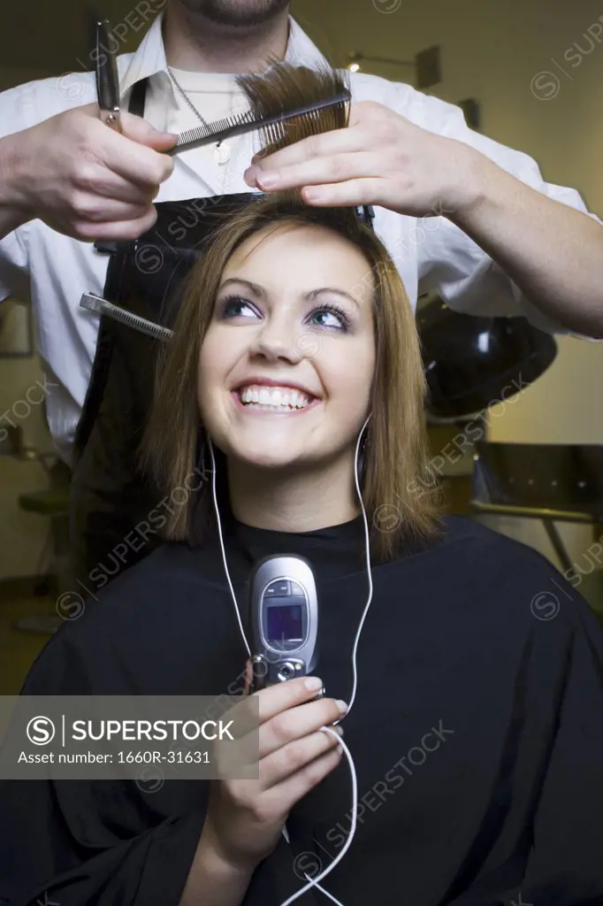 Young woman listening to music on cell phone at hairdresser's