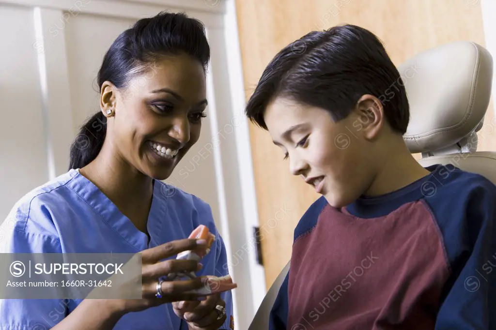 Dental hygienist holding false teeth talking to boy