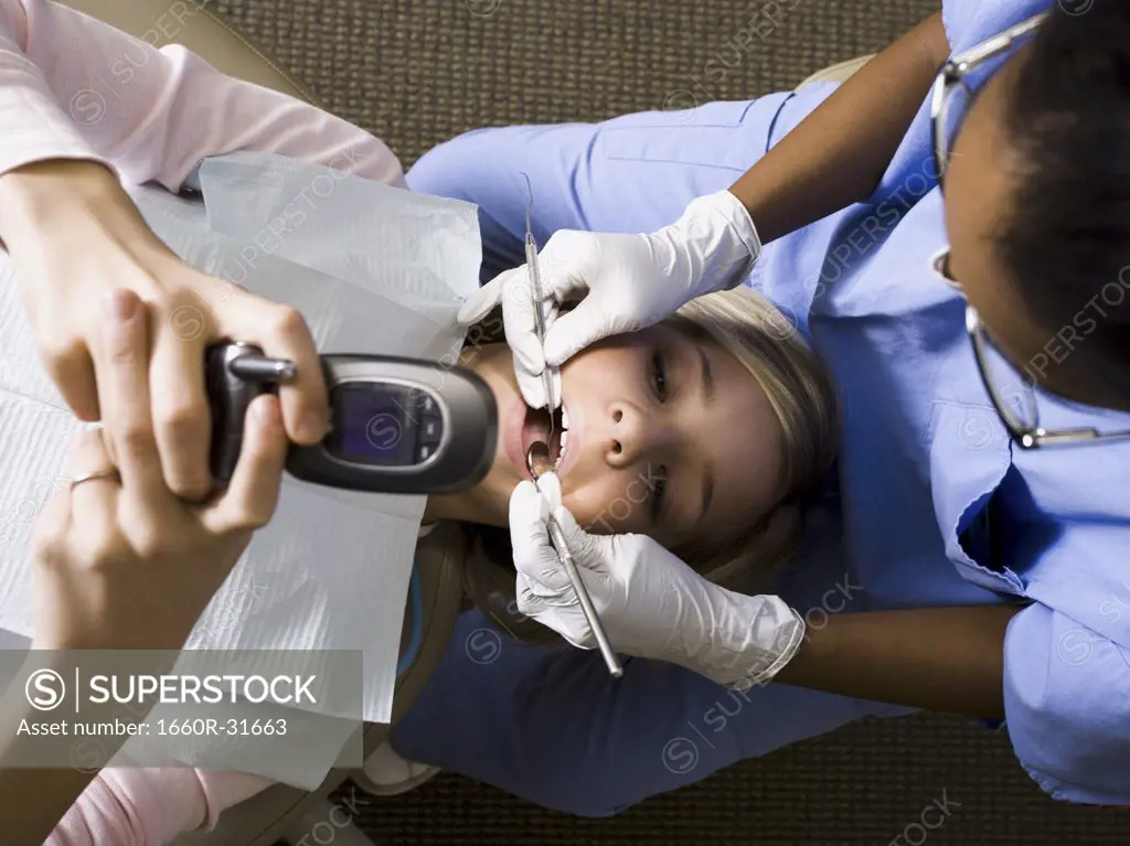 Girl having dental exam holding cell phone