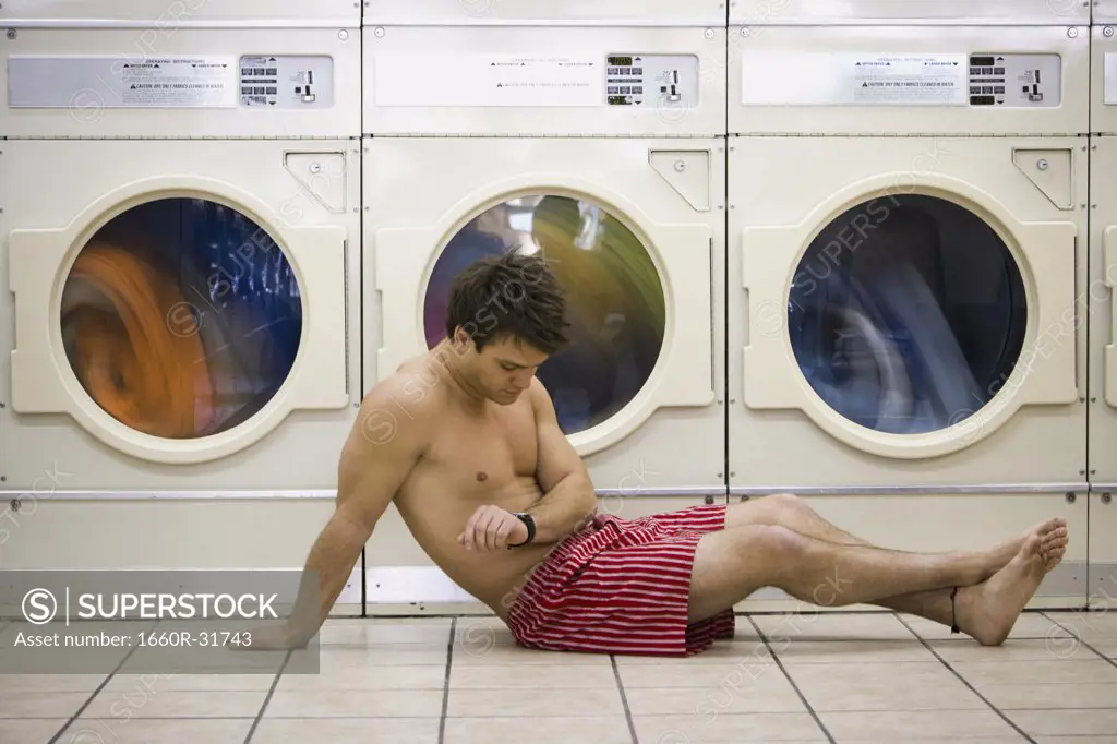 Man sitting in boxers at Laundromat checking watch