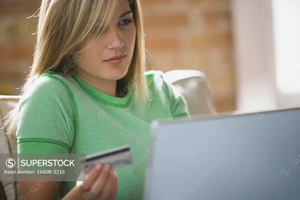 Close-up of a teenage girl holding a credit card sitting in front of a laptop