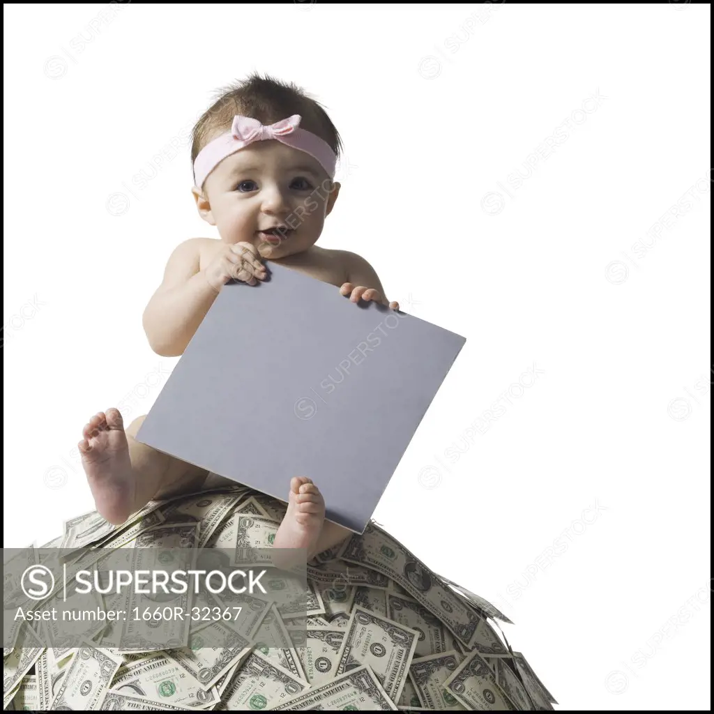 Baby girl sitting on pile of US currency with blank sign