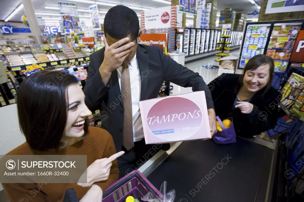 Man at grocery checkout with box of tampons and two women