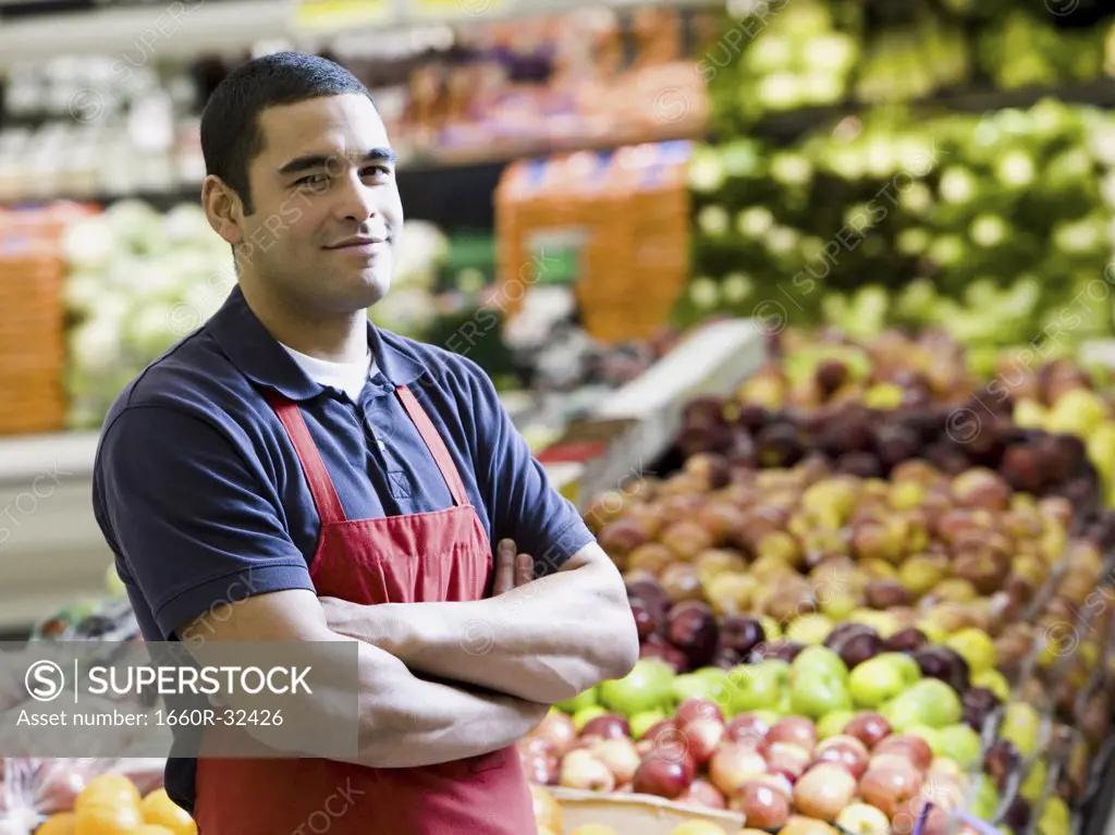 Man with apron in grocery store with arms crossed