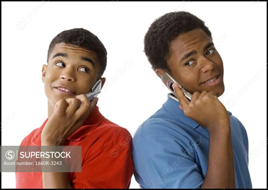 Close-up of two young men standing back to back talking on mobile phones