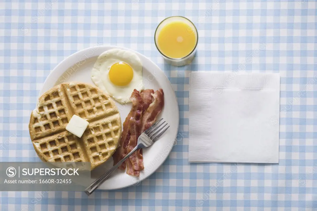 Bacon and eggs with waffle and orange juice with napkin and fork
