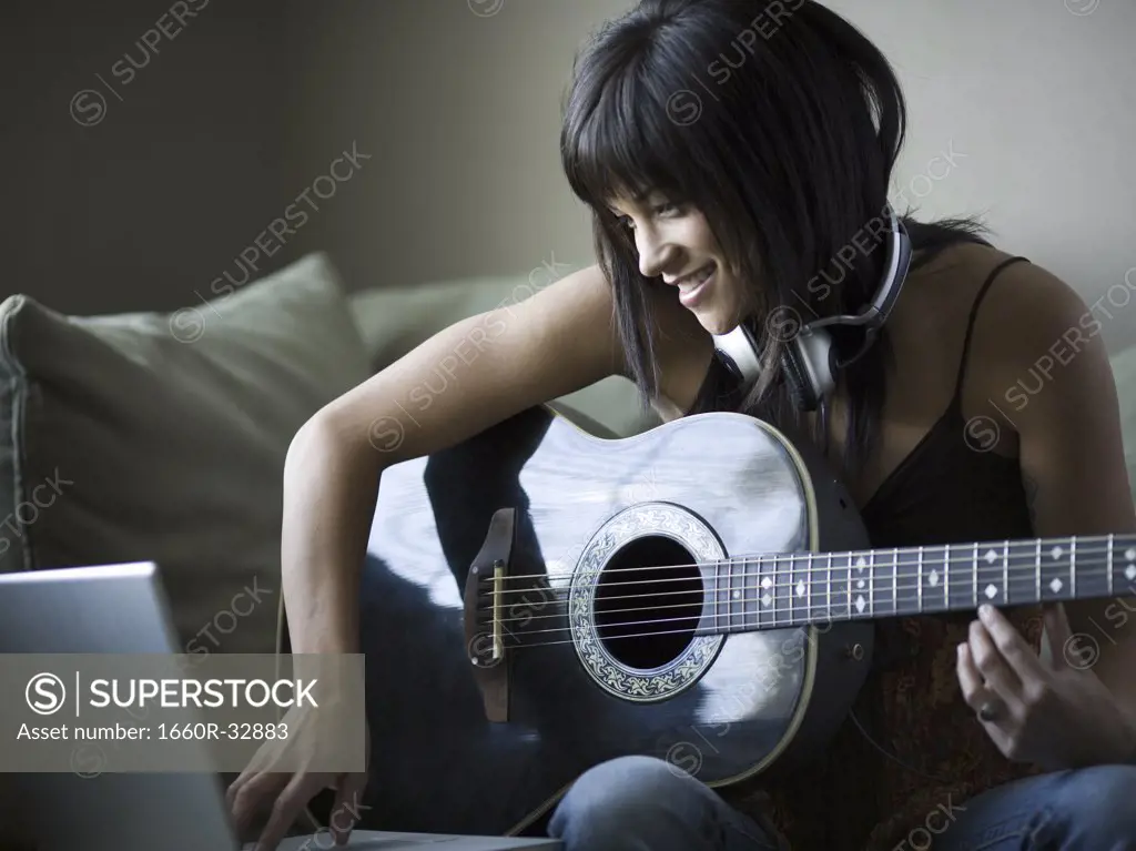 Woman sitting on sofa with laptop and guitar