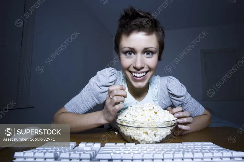 Woman sitting at keyboard with bowl of popcorn