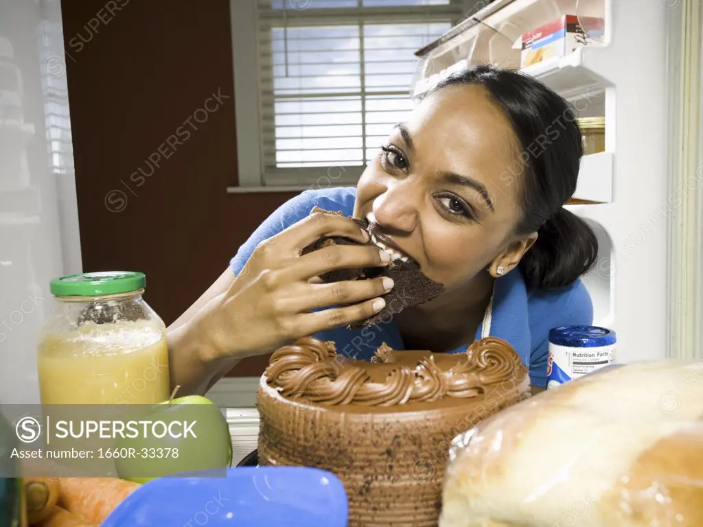 Woman devouring chocolate cake from refrigerator