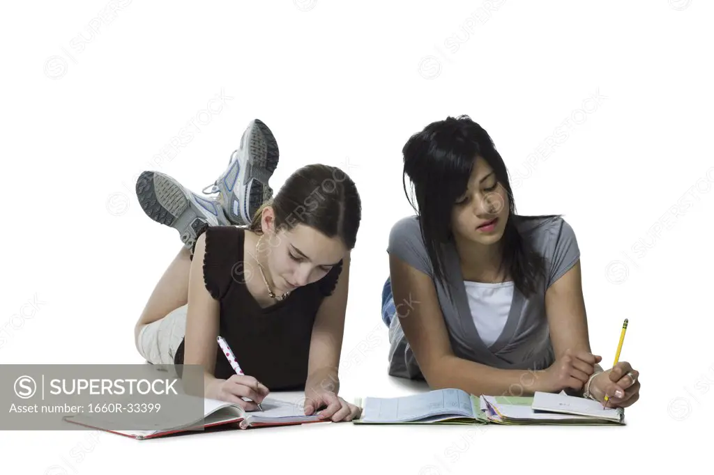 Two girls lying down doing homework