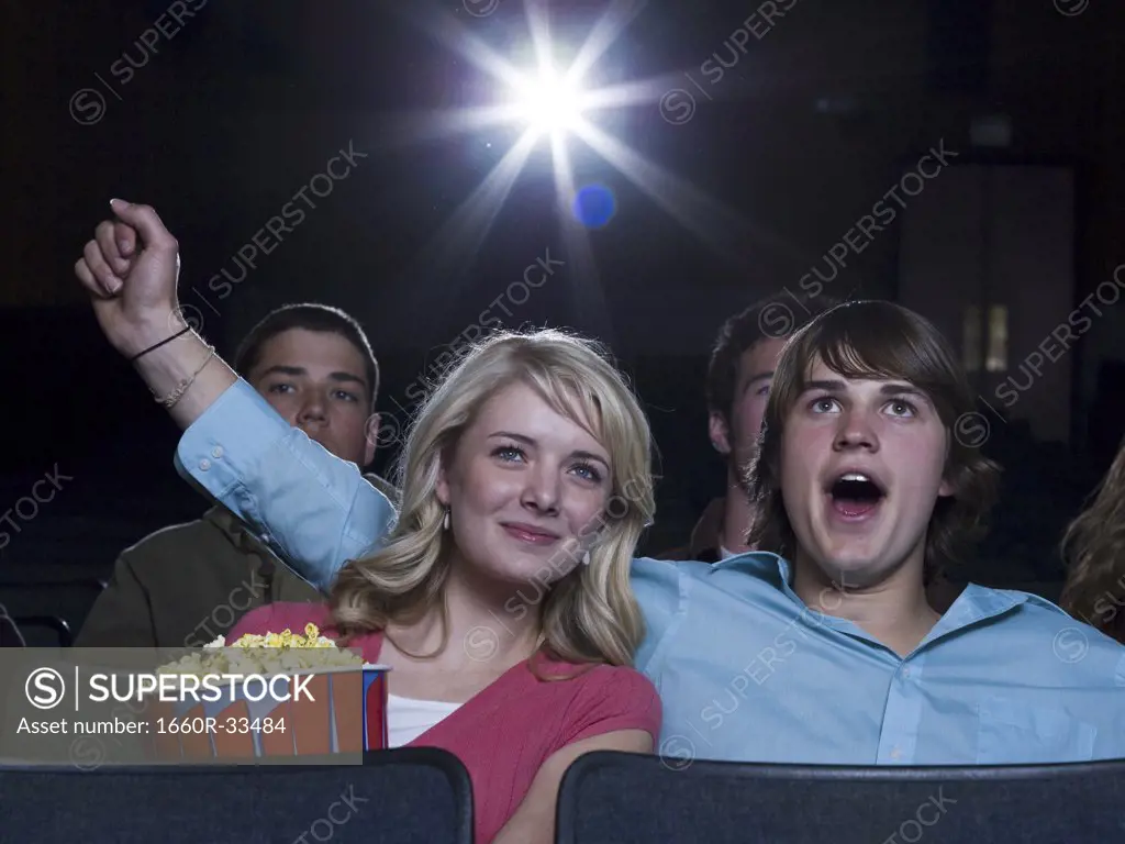 Boy reaching arm out behind girl with popcorn at movie theater