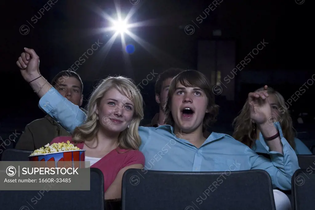 Boy reaching arm out behind girl with popcorn at movie theater