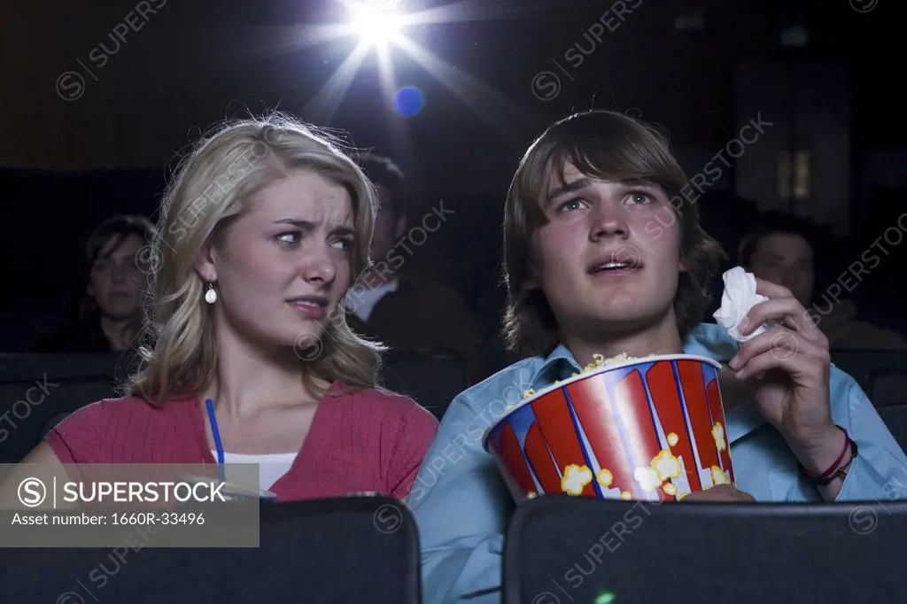 Boy with tissues crying at movie theater with girl watching
