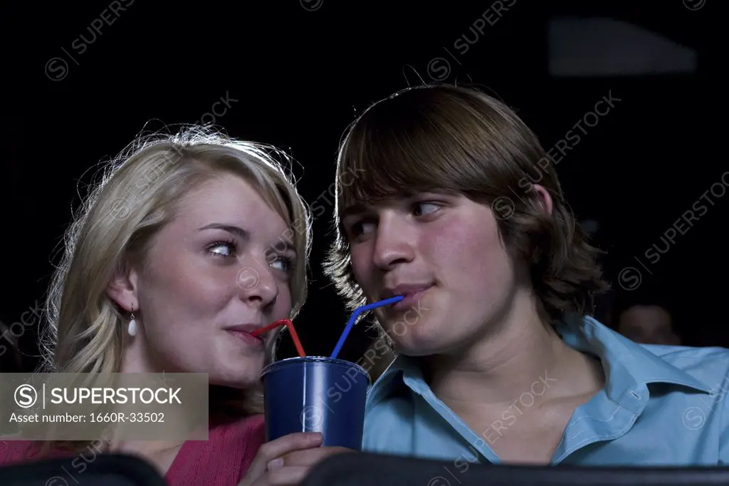 Boy and girl sharing beverage at movie theater