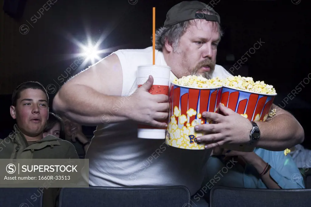 Large man with buckets of popcorn and drink at movie theater