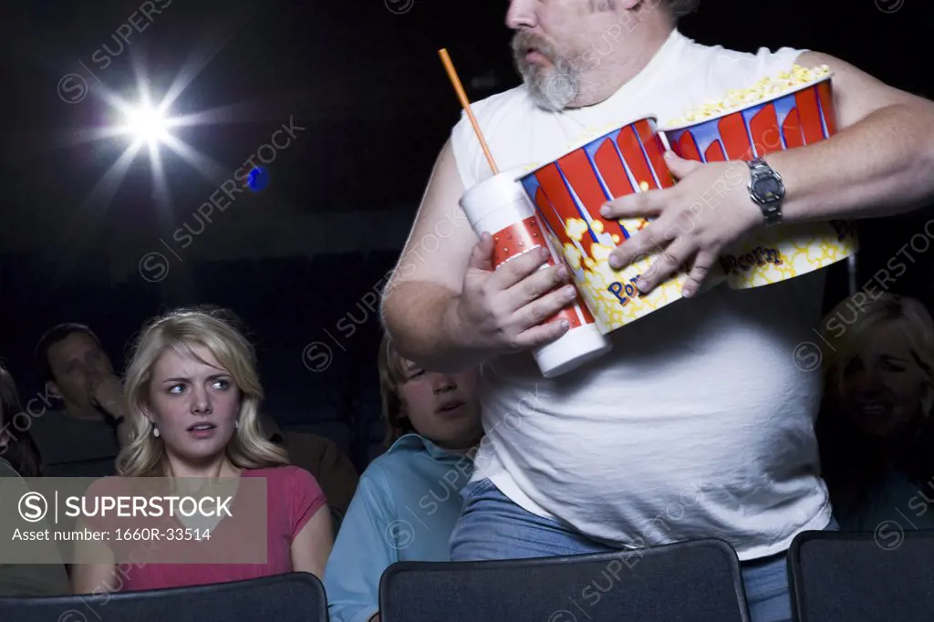 Large man with buckets of popcorn and drink at movie theater