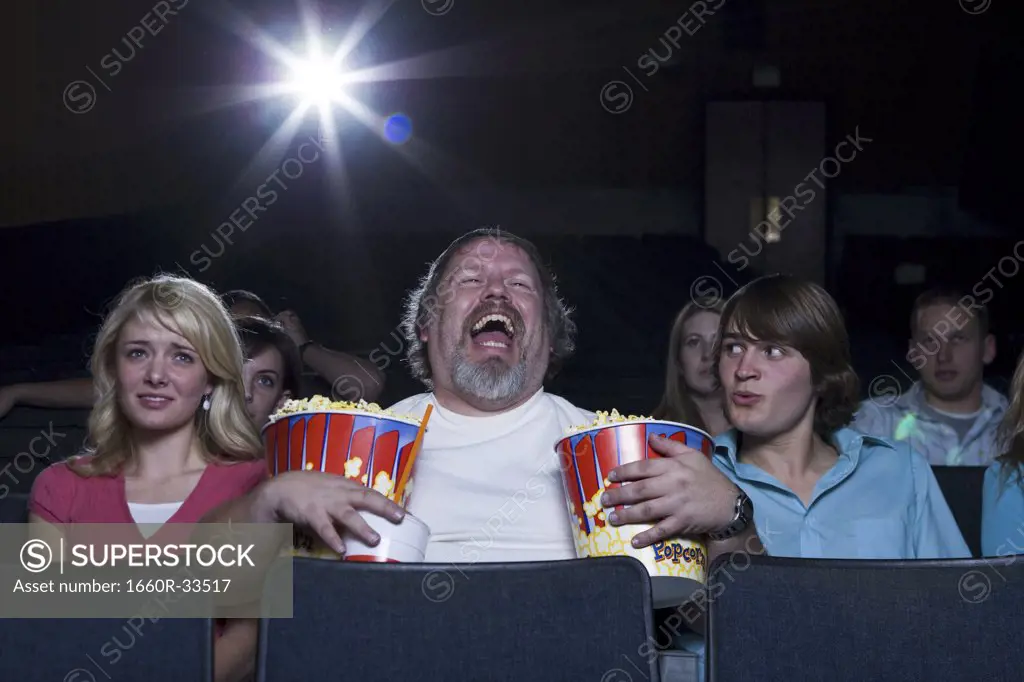 Large man with buckets of popcorn and drink at movie theater between couple
