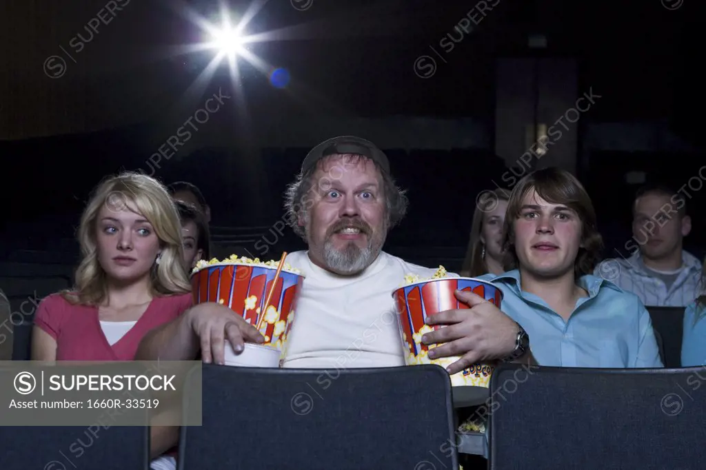 Large man with buckets of popcorn and drink at movie theater between couple