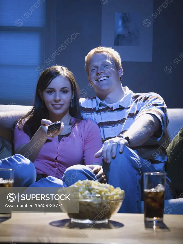 Couple with bowl of popcorn watching television smiling