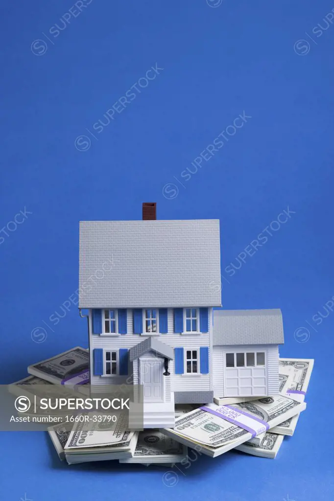 Toy house on pile of one hundred dollar bills